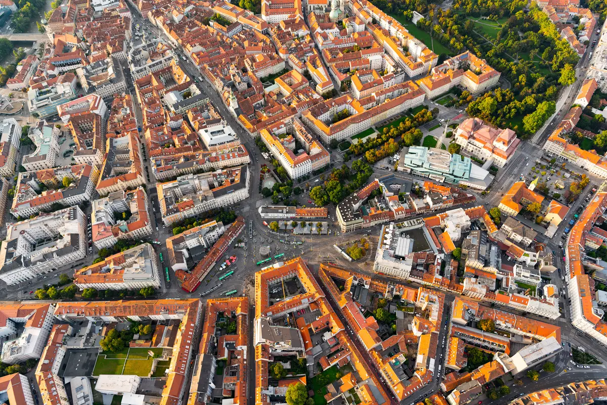 Graz seen from above: red-tiled roofs of the old town, a large square crossed by tram lines, a park in the top right corner